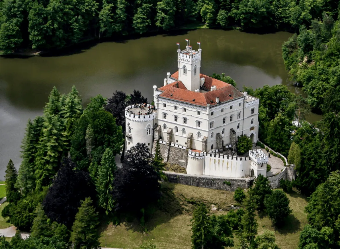 Pogled iz zraka na dvorac Trakošćan, okružen šumom uz jezero.